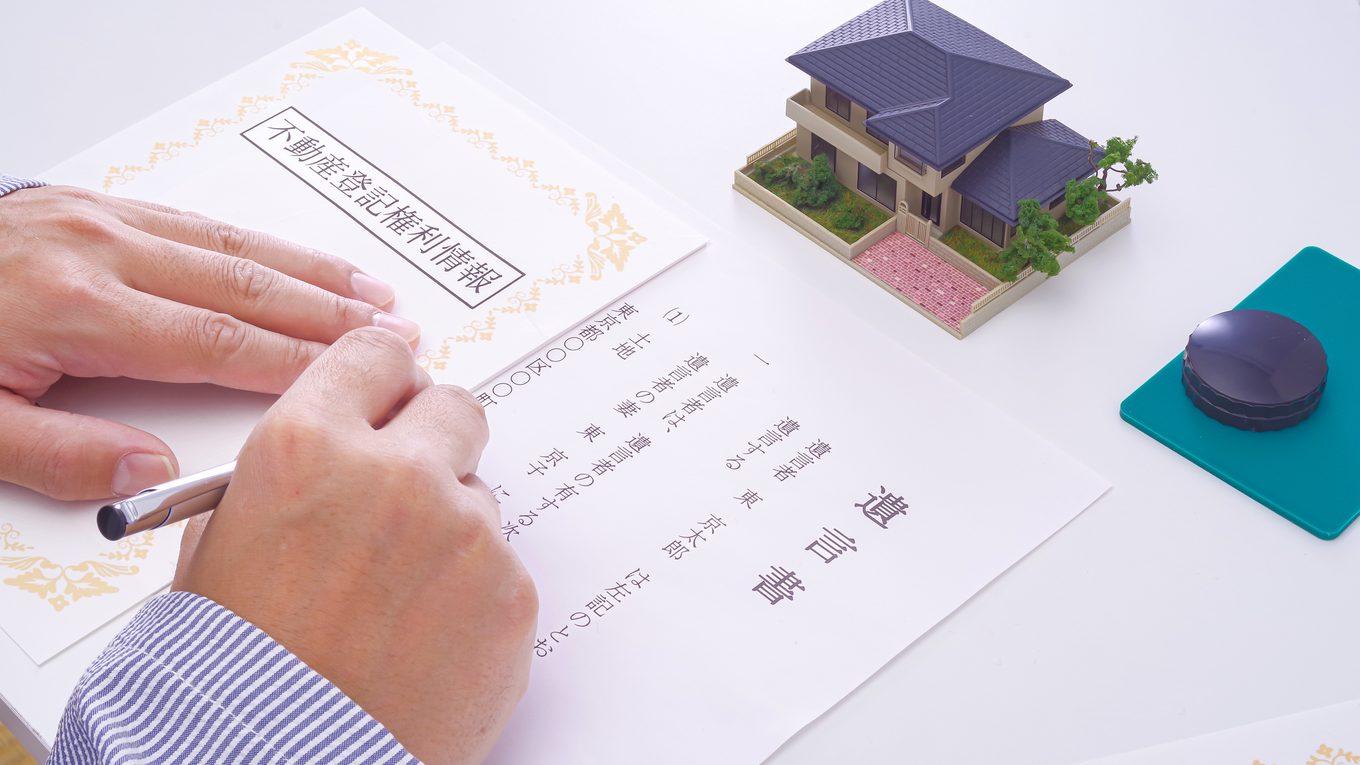 遺言書を自筆で書き直しているところ。机には不動産の登記権利情報と印鑑が置かれている